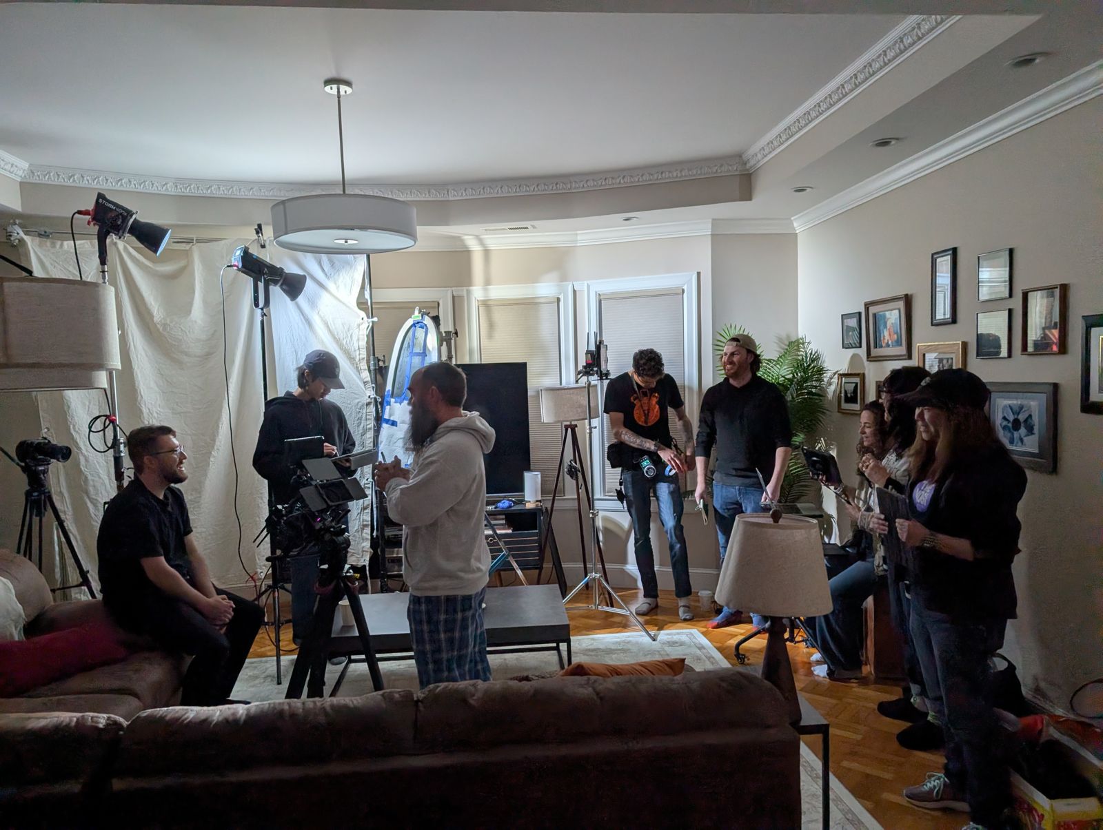 A living room converted into a film set, with lights, a camera rig, and crew working around a seated subject