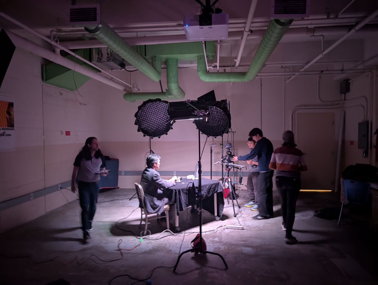 A dim basement room set up for a tabletop shoot, with two softboxes over a table and crew adjusting the camera