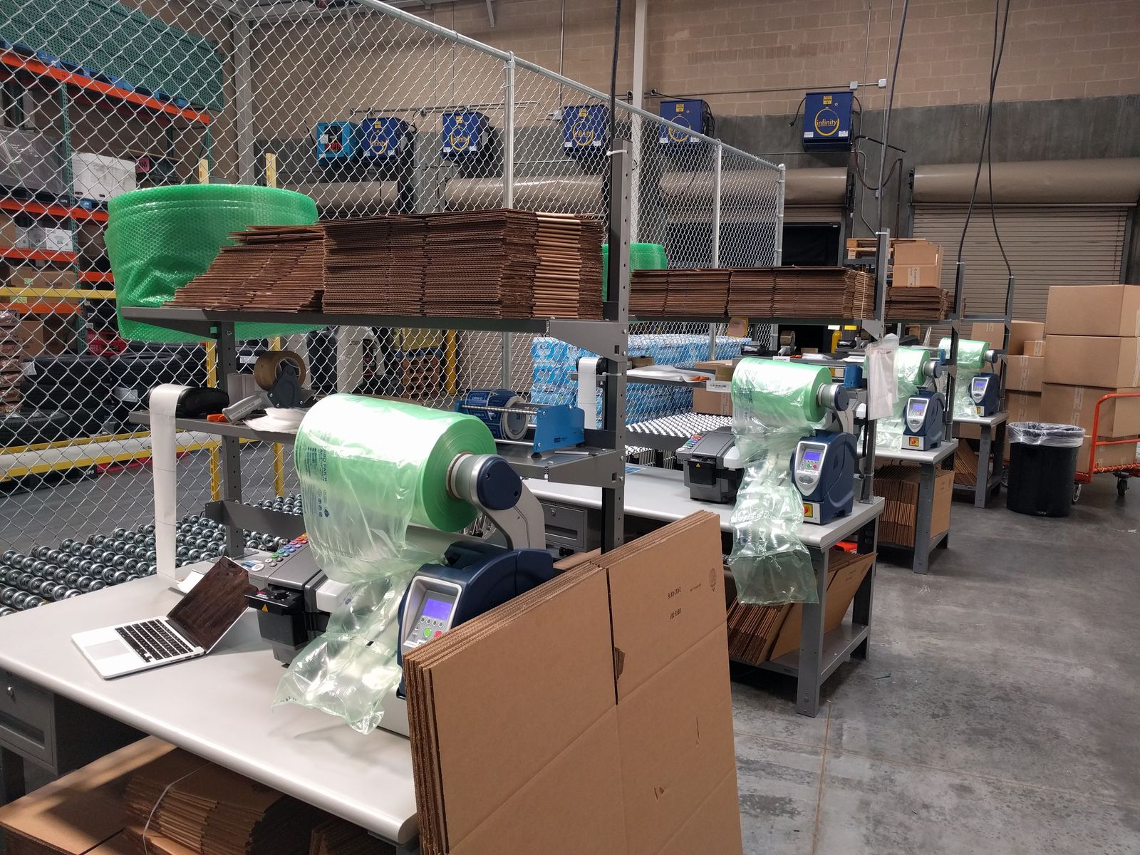 A row of packing stations with box blanks and green bubble wrap