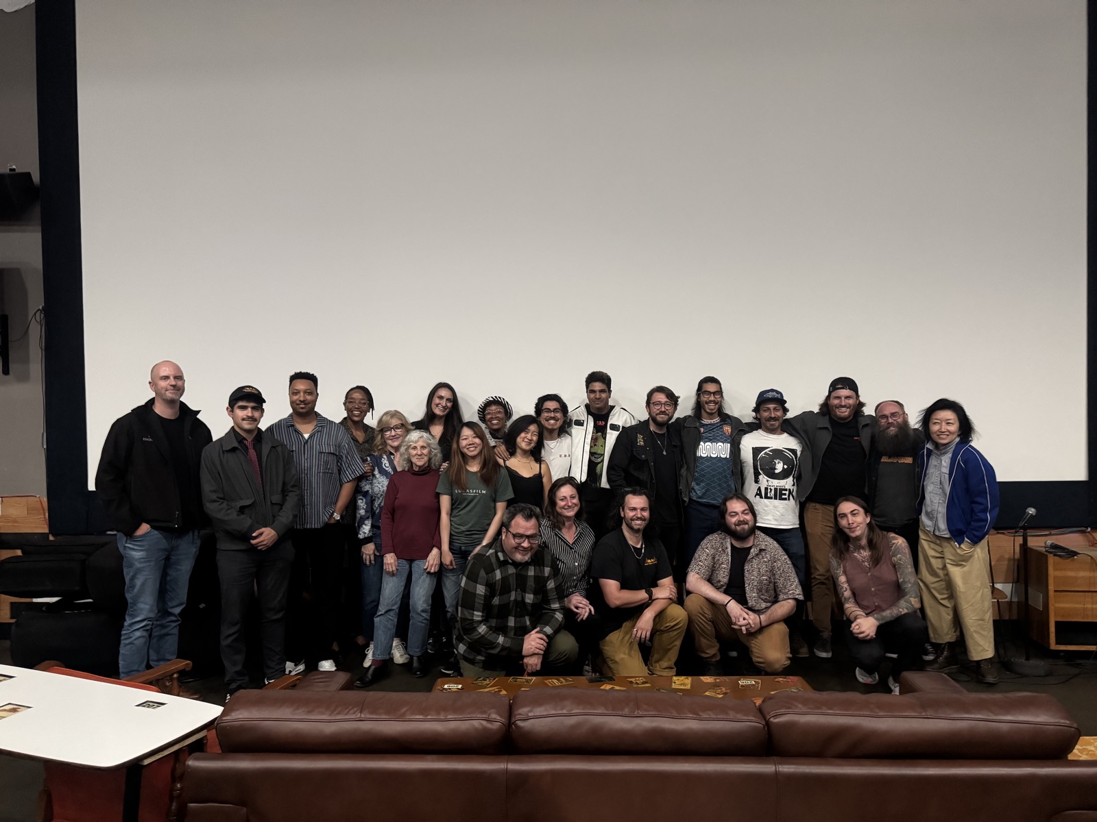 The cast and crew of Slumped Over Man standing and kneeling in front of the theater screen after the premiere